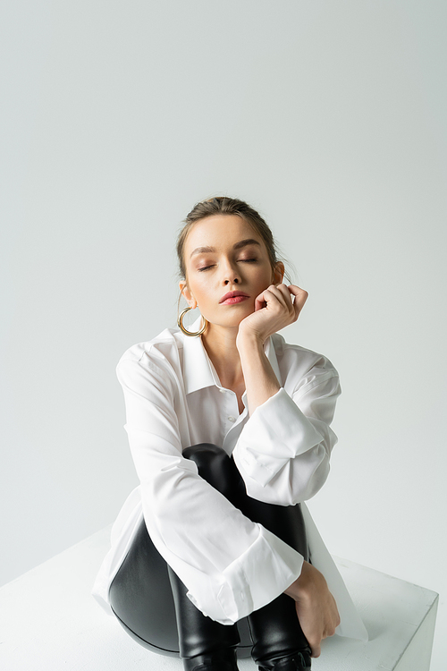 stylish woman in white shirt and black tight pants sitting with closed eyes isolated on grey