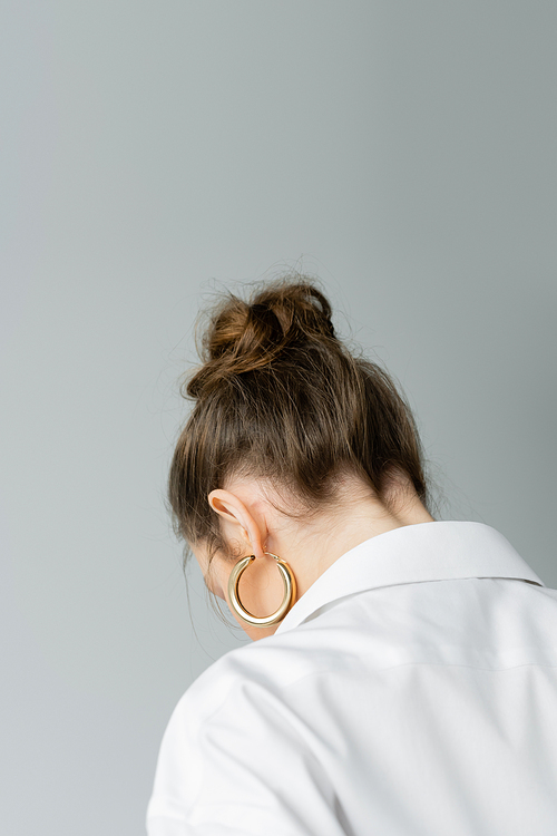 back view of young woman in golden hoop earring and white shirt isolated on grey