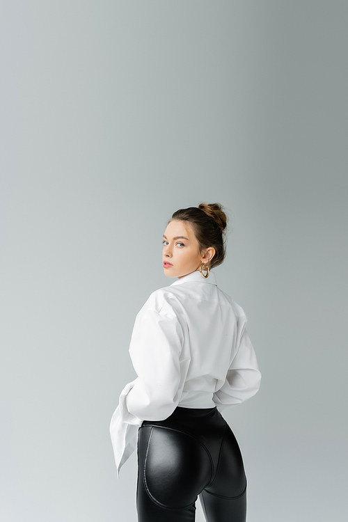 sexy woman in white shirt and black tight pants looking at camera isolated on grey