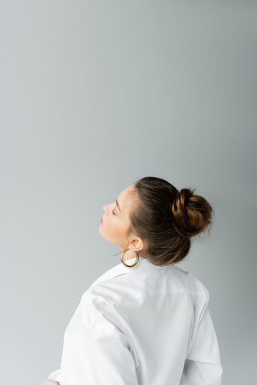 young model in white shirt and hoop earring posing isolated on grey with copy space