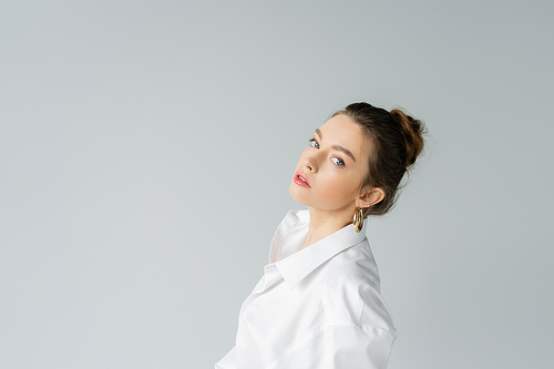 portrait of young model in white oversize shirt looking at camera isolated on grey