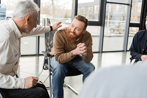 Mature man comforting smiling person with alcohol addiction in rehab center