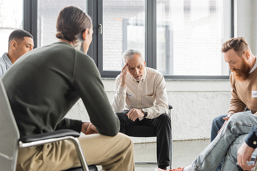 Upset mature man with alcohol addiction sitting in circle during therapy in rehab center