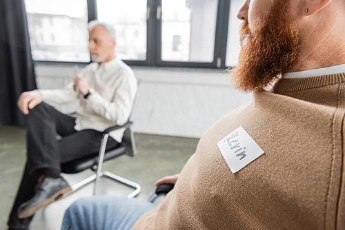 Bearded man with name sticker sitting at group therapy session in rehab center