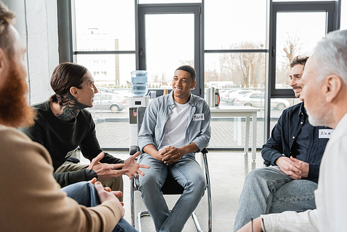 Tattooed man with alcohol addiction talking to multiethnic group in rehab center