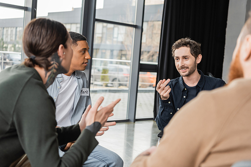 Interracial people with alcohol addiction talking during group therapy in rehab center