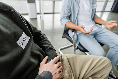 Cropped view of man with name sticker sitting in circle during alcoholics meeting in rehab center