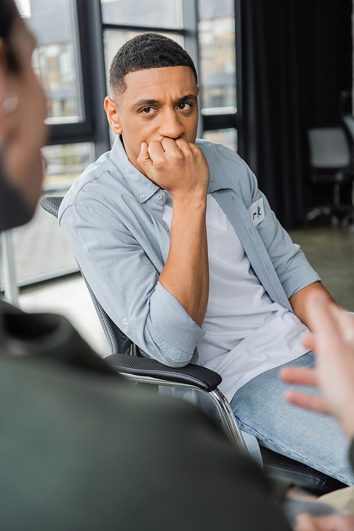 Worried african american man with alcohol addiction listening story during therapy in rehab center