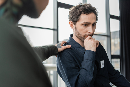 Blurred man calming person with alcohol addiction during meeting in rehab center