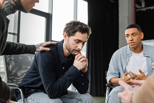 Multiethnic people calming upset person during alcoholics meeting in rehab center