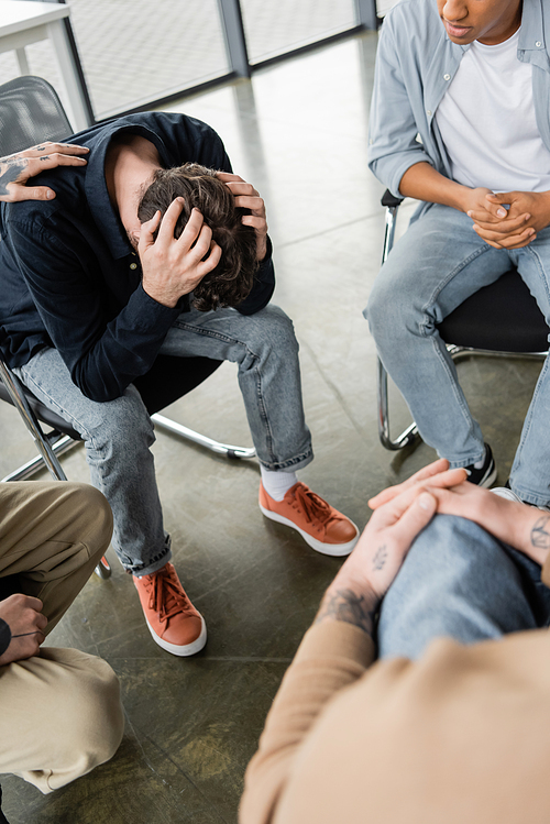 Interracial group calming depressed person with alcohol addiction in rehab center