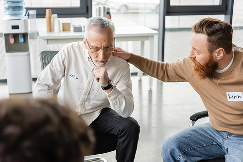 Man calming mature person with alcohol addiction during group therapy session in rehab center