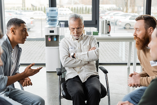 Sad middle aged man sitting near interracial people at alcoholics meeting in rehab center