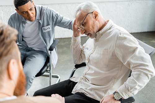 Displeased man with alcohol addiction sitting near interracial people in rehab center