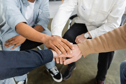 Cropped view of interracial people sitting in circle and putting hands together during alcoholics meeting in rehab center