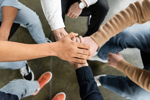 Top view of multiethnic group of people with alcohol addiction holding hands together in rehab center