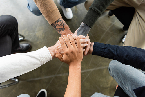 Top view of multiethnic people holding hands together during anonymous alcoholics meeting in rehab center