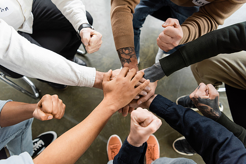 Top view of interracial people with alcohol addiction holding hands and showing yes gesture in rehab center