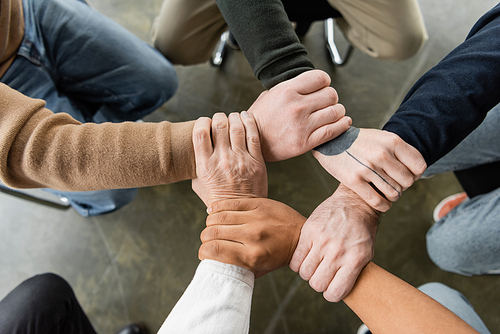 Top view of multiethnic people with alcohol addiction joining hands during group therapy in rehab center