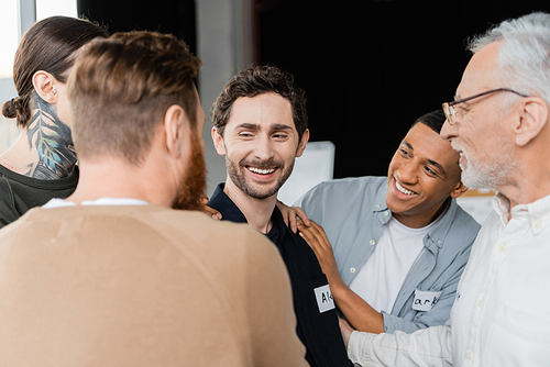 Positive multiethnic group supporting smiling man during alcoholics meeting in rehab center