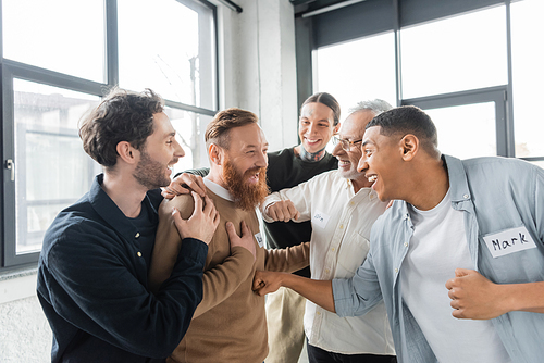 Interracial people hugging cheerful man during alcoholics meeting in rehab center