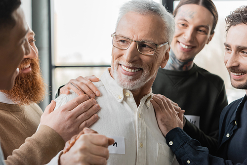 Cheerful interracial people hugging mature member of alcoholics in rehab center