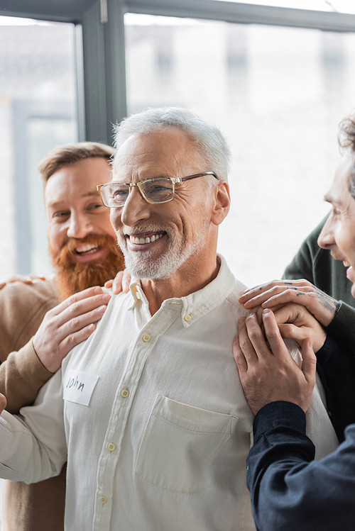 Positive people hugging middle aged man with alcohol addiction during group therapy in rehab center