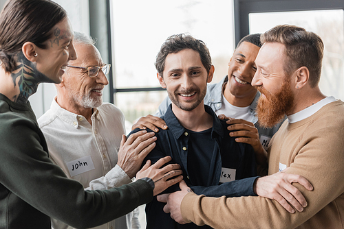 Multiethnic people hugging smiling man with alcohol addiction during group therapy in rehab center