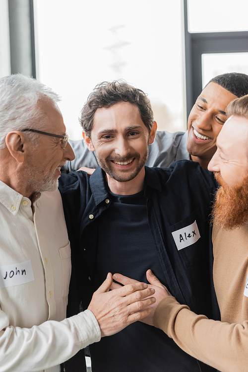 Interracial people hugging cheerful man during alcoholics therapy in rehab center