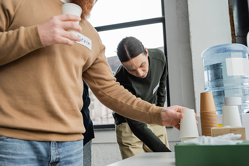 Tattooed man standing near water cooler during alcoholics meeting in rehab center