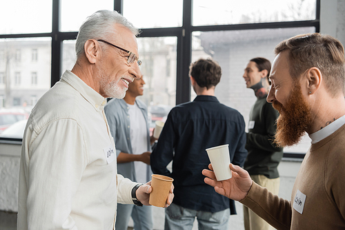 Smiling men with paper cups talking during alcoholics meeting in recovery center