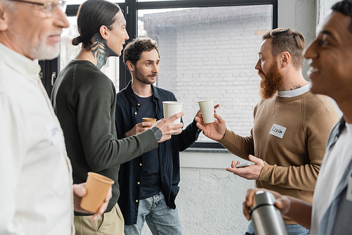 Interracial people with alcohol addiction talking and holding paper cups in recovery center