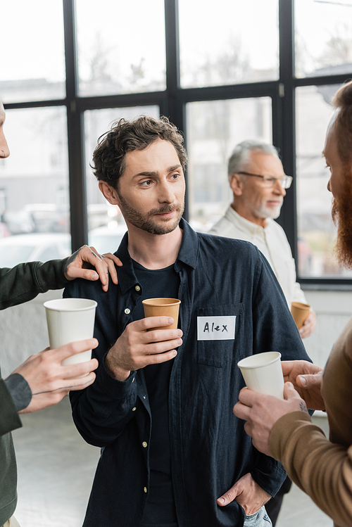 People with paper cups talking to man during alcoholics meeting in rehab center