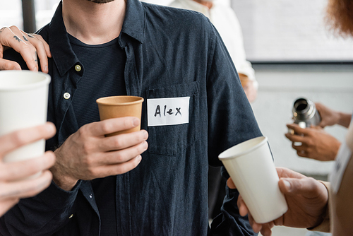 Cropped view of people holding paper cups during alcoholics meeting in recovery center