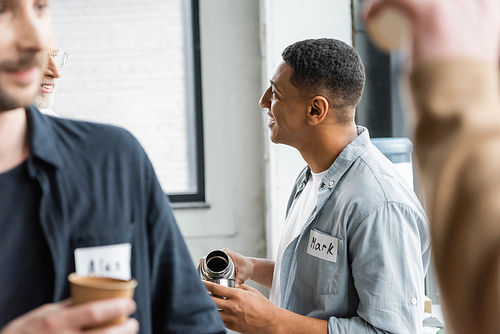 Smiling african american man pouring drink from thermos and talking during alcoholics meeting in rehab center