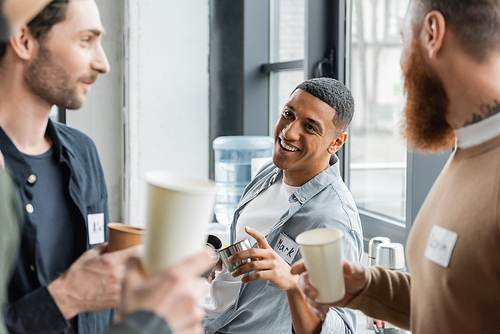 Cheerful african american man holding thermos and talking to people during alcoholics meeting in rehab center