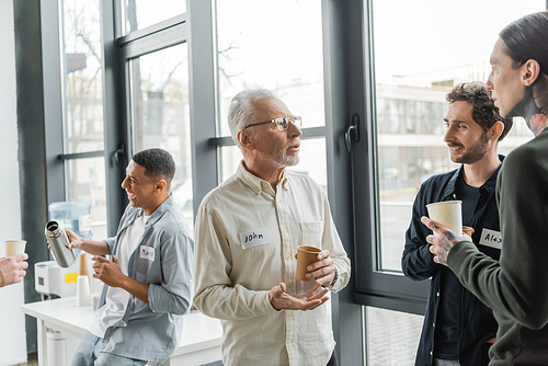 Mature man with alcohol addiction holding paper cup and talking to people in recovery center