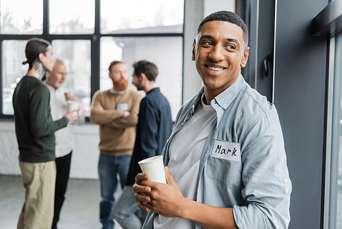 Positive african american man with alcohol addiction holding paper cup in recovery center