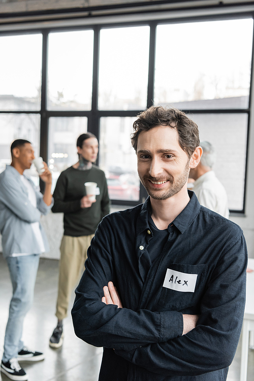 Positive man with name sticker crossing arms during alcoholics meeting in recovery center