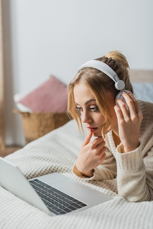 focused woman in wireless headphones watching movie on laptop in bedroom