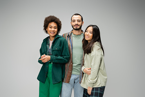 young and happy multicultural friends in stylish casual clothes looking at camera isolated on grey