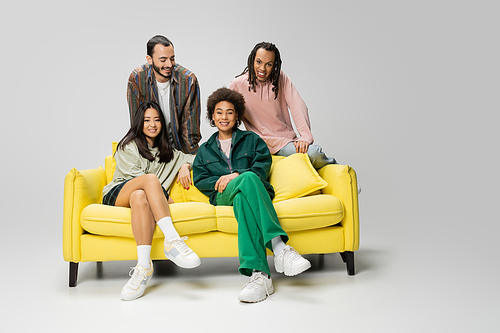 cheerful african american women sitting on yellow couch near trendy multiethnic men on grey background