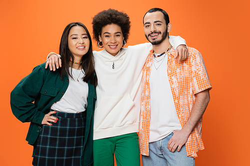 cheerful african american woman embracing trendy multiracial friends isolated on orange
