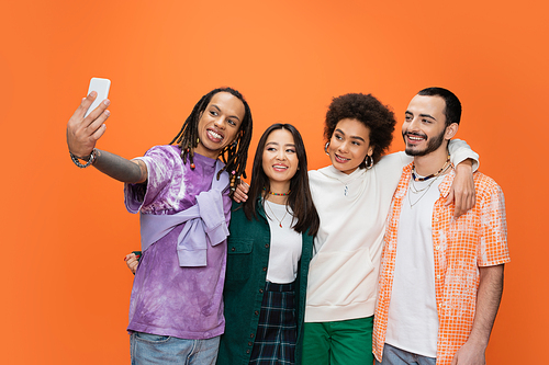 cheerful man with dreadlocks taking selfie with young multicultural friends isolated on orange