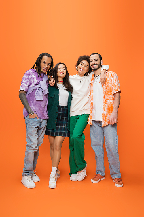 full length of happy african american woman embracing stylish multicultural friends on orange background