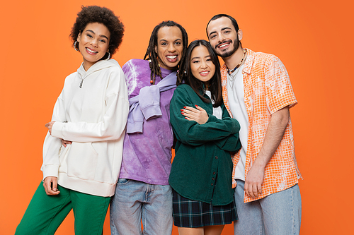 happy multiethnic friends wearing stylish clothes and posing isolated on orange
