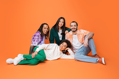 multicultural friends in trendy casual attire smiling while posing on orange background