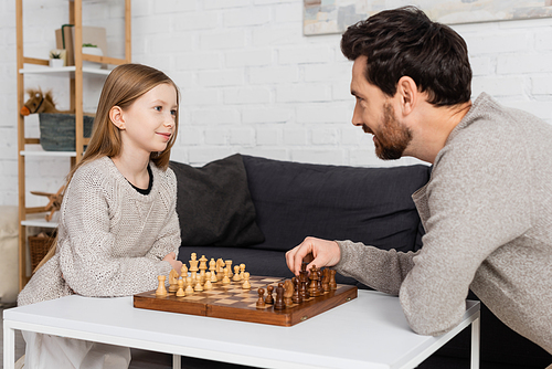 preteen girl smiling while playing chess with bearded dad at home