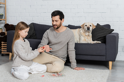 preteen girl wearing ring on finger of father while playing on floor near labrador dog lying on couch in living room