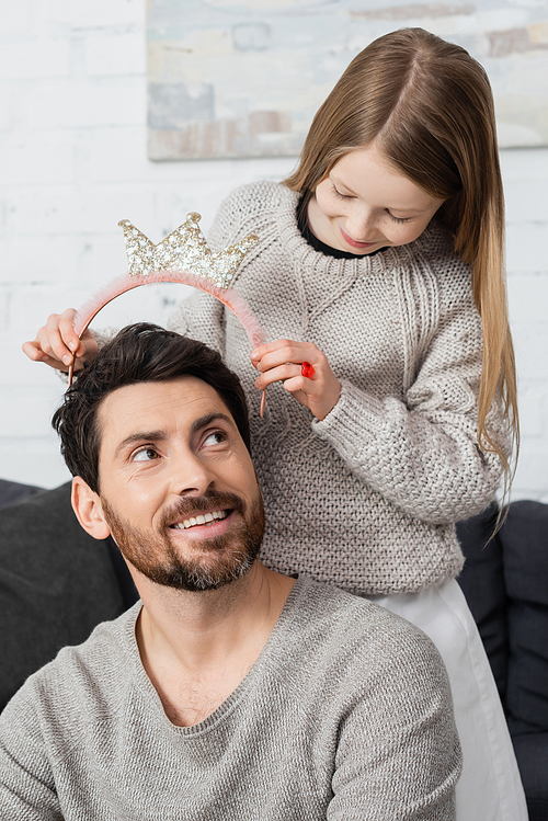 happy preteen girl wearing crown on head of joyful father with beard